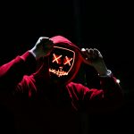 A spooky illuminated mask figure with a red hoodie in a dark setting, perfect for Halloween themes.